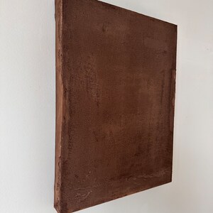 May include: A square brown canvas painting with a textured surface.