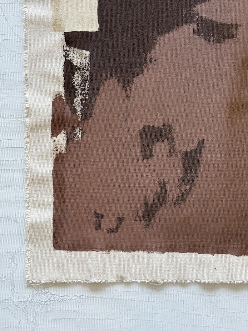 May include: Abstract art piece featuring a canvas with a raw edge. The artwork uses a palette of brown and beige tones, with brushstrokes and shapes creating a textured effect. The canvas is mounted on a white surface.