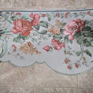 May include: Floral wallpaper border featuring large pink roses, smaller red flowers, and green leaves on a light blue background. The border has a scalloped edge with a green trim.