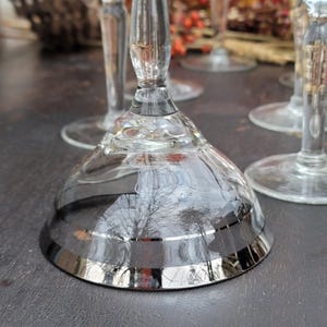 May include: Set of four clear glass stemmed cocktail glasses with a silver rim. The glasses have a delicate design and are perfect for serving cocktails or other beverages.