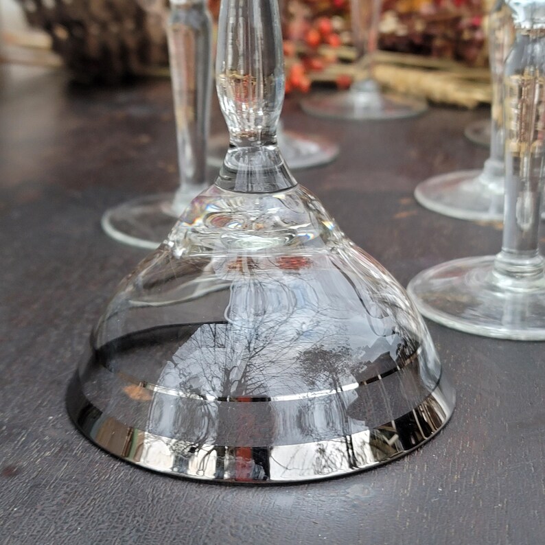 May include: Set of four clear glass stemmed cocktail glasses with a silver rim. The glasses have a delicate design and are perfect for serving cocktails or other beverages.