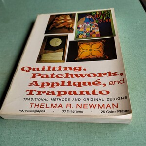 May include: A book titled "Quilting, Patchwork, Appliqué, and Trapunto" by Thelma R. Newman. The cover features images of quilts and a decorative pillow. The book details traditional methods and original designs, with 400 photographs, 30 diagrams, and 26 color plates.