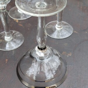 May include: Three clear glass stemmed cocktail glasses with a silver rim. The glasses are on a dark brown surface.