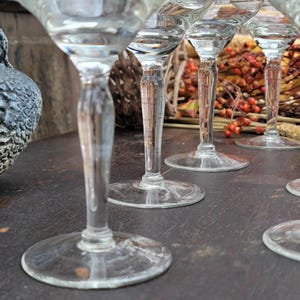 May include: A set of six clear glass martini glasses with a stem and a wide bowl. The glasses are arranged in a row on a dark wooden surface.
