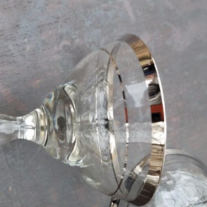 May include: Two clear glass cocktail glasses with a silver rim. The glasses are on a gray surface.