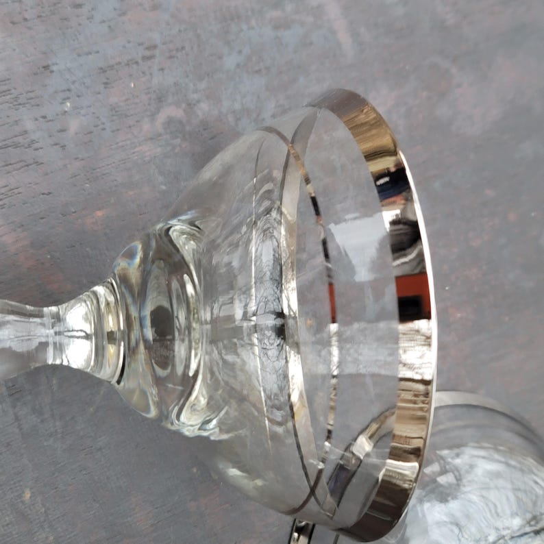 May include: Two clear glass cocktail glasses with a silver rim. The glasses are on a gray surface.