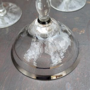 May include: A clear glass goblet with a silver rim on the base. The goblet is reflecting the surrounding environment.