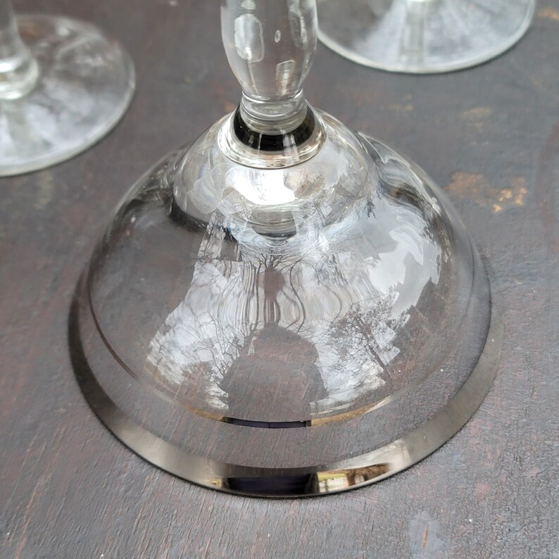 May include: A clear glass goblet with a silver rim on the base. The goblet is reflecting the surrounding environment.