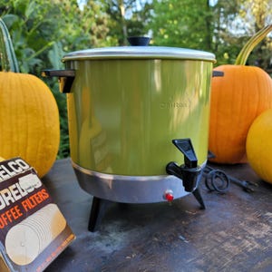 May include: Vintage green Chilton coffee urn with a silver rim, black spout, and legs. The urn has a black handle and lid. A box of coffee filters is next to the urn, with pumpkins in the background.