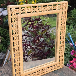 May include: A rectangular wall mirror featuring a light tan woven wicker frame. The frame displays an intricate, repeating lattice pattern along its outer border, surrounding a central glass mirror pane with a smooth, light-colored finish.