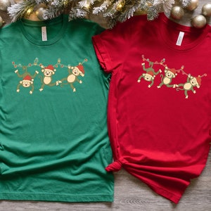 May include: Two t-shirts featuring a Christmas monkey design. The green shirt has the text "Kelly Green" and the red shirt has the text "Red".