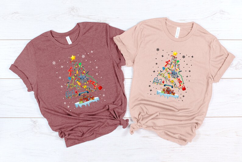 May include: Two t-shirts with a Christmas tree design made of fitness equipment. The tree is decorated with ornaments and a star on top. The t-shirts are in maroon and light pink.