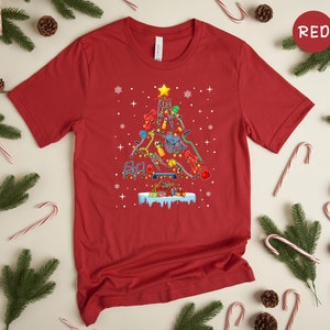 May include: Red t-shirt with a Christmas tree design made of fitness equipment. The tree is decorated with lights and ornaments. The text "RED" is in the upper right corner of the image.