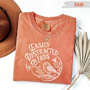 a red t-shirt with a white bird design and text, a brown hat, and a fan, all arranged on a white background.