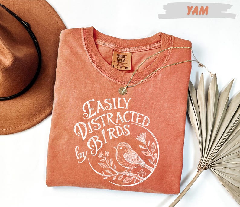 a red t-shirt with a white bird design and text, a brown hat, and a fan, all arranged on a white background.