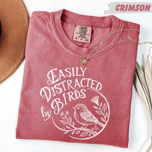 a red t-shirt with a white graphic design, a brown hat, and some dried leaves, all arranged on a white background.