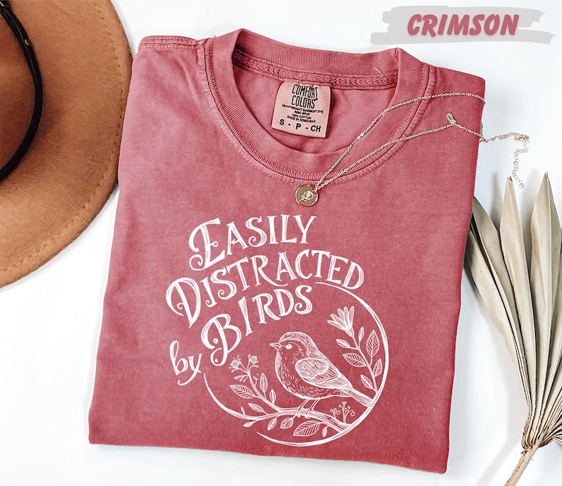 a red t-shirt with a white graphic design, a brown hat, and some dried leaves, all arranged on a white background.