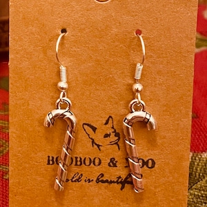 May include: Silver candy cane earrings displayed on a brown card with the text "BOOBOO & JOO" and "old is beautiful". The earrings have a spiral design and are suspended from silver hooks.