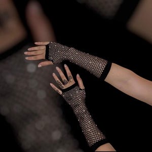 May include: Black fishnet gloves with sparkling embellishments. The gloves are fingerless, extending from the wrist to the mid-upper arm. The background is dark, emphasizing the gloves' texture and design. A stylish accessory for various occasions.