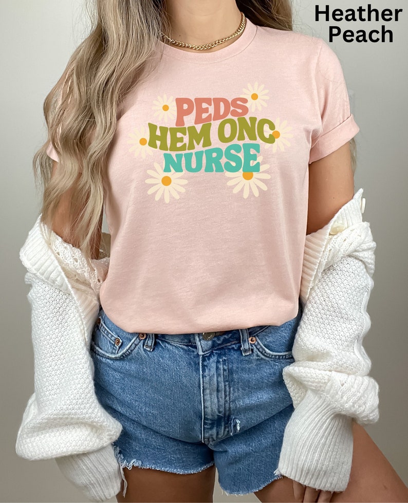 May include: A heather peach t-shirt with the text "PEDS HEM ONC NURSE" in colorful letters and daisy flowers around the text.