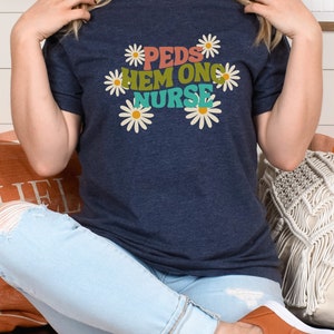 May include: A navy blue t-shirt with a graphic design of daisies and the text "PEDS HEM ONC NURSE" in colorful letters.