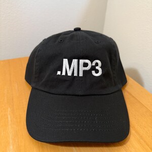 May include: Black baseball cap with a curved brim. The cap features the white text ".MP3" embroidered on the front. The hat is made of a durable fabric and has an adjustable strap at the back.