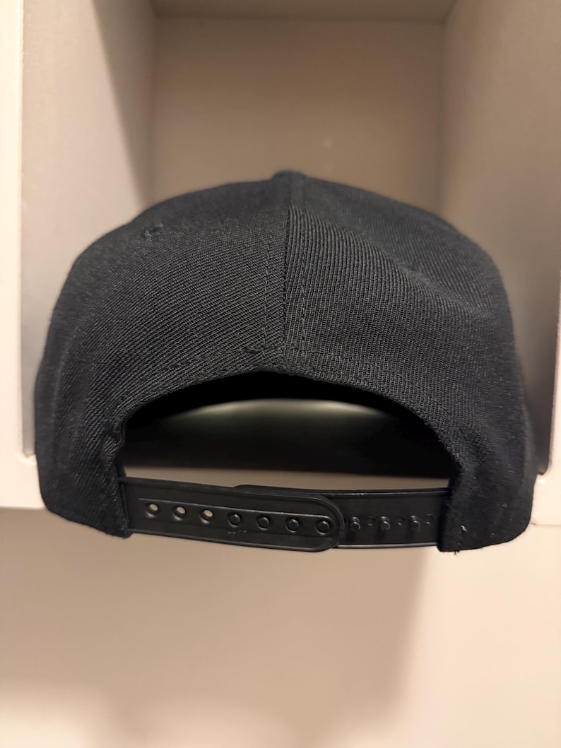 May include: A black snapback baseball cap. The cap features a structured crown and a flat brim. The adjustable strap on the back allows for a customized fit. The cap is made of a durable fabric.