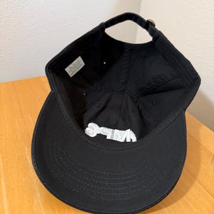 May include: Black baseball cap with a curved brim and adjustable strap. The interior features a white label and white embroidered text. The cap is made of a soft, durable fabric.