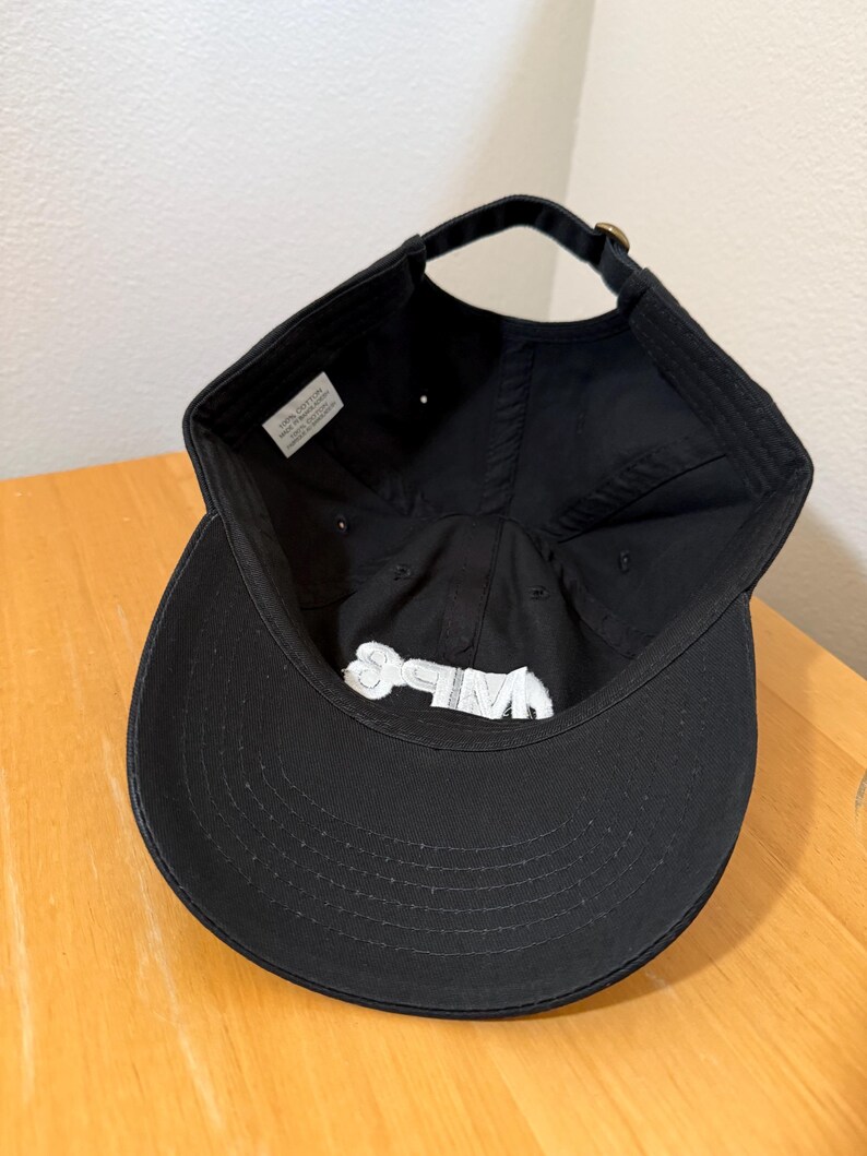 May include: Black baseball cap with a curved brim and adjustable strap. The interior features a white label and white embroidered text. The cap is made of a soft, durable fabric.