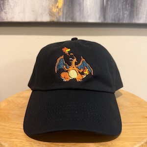 May include: A black baseball cap with an embroidered image of a cartoon orange and red dragon with blue wings and yellow flames. The dragon is breathing fire.