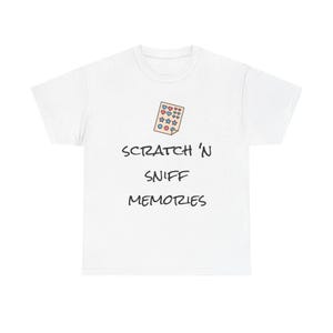 Puede incluir: Camiseta blanca con el texto "SCRATCH 'N SNIFF MEMORIES" en fuente negra. Encima del texto hay una pequeña ilustración de una tarjeta rasca y huele con formas de corazón, estrella y círculo en rosa, azul y amarillo.