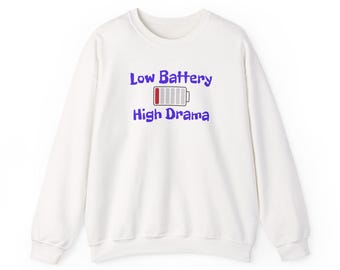 Puede incluir: Sudadera blanca de cuello redondo con el texto "Low Battery High Drama" en azul. El diseño incluye un icono de batería con relleno rojo, que indica poca energía. Una prenda superior informal y cómoda.