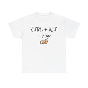 Puede incluir: Camiseta blanca con el texto "CTRL + ALT + NAP" en escritura negra. Una ilustración de dibujos animados de un perro durmiendo está debajo del texto. La camiseta es de un material suave.
