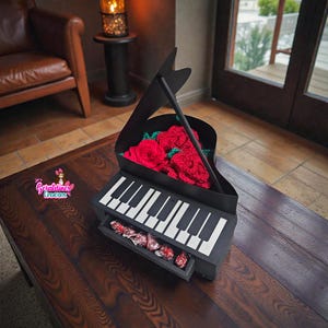 Może przedstawiać: Czarne pudełko na prezent w kształcie fortepianu z czarno-białym wzorem klawiatury. Pudełko zawiera czerwone szydełkowe róże i szufladę wypełnioną zapakowanymi cukierkami. Pudełko stoi na ciemnym drewnianym stole.