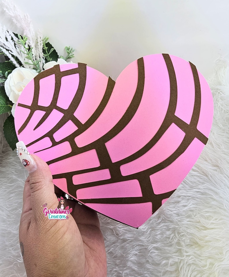 May include: A pink and brown heart-shaped box with a decorative pattern resembling a traditional Mexican sweet bread, "Conchas".