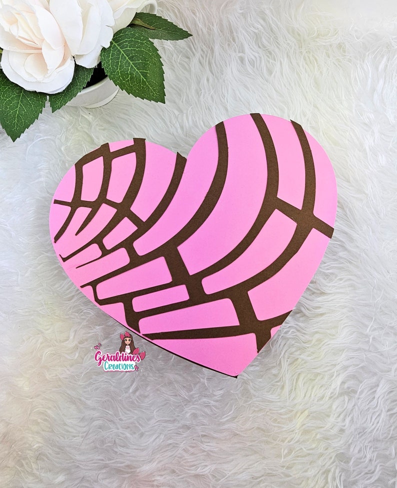 May include: A pink and brown heart-shaped box with a pattern resembling a traditional Mexican sweet bread, "Conchas". The box is on a white fluffy surface. The text "Geraldines Creations" is visible at the bottom of the image.