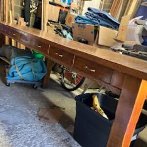 May include: A long, wooden table with six drawers and a dark brown finish. The table has a rustic, farmhouse style and is perfect for a dining room or kitchen.