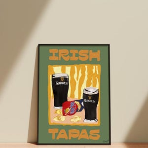 May include: A framed art print depicting two pints of Guinness and a packet of Tayto crisps. The words "IRISH TAPAS" are printed in orange block letters on a green background. The art has a minimalist style.