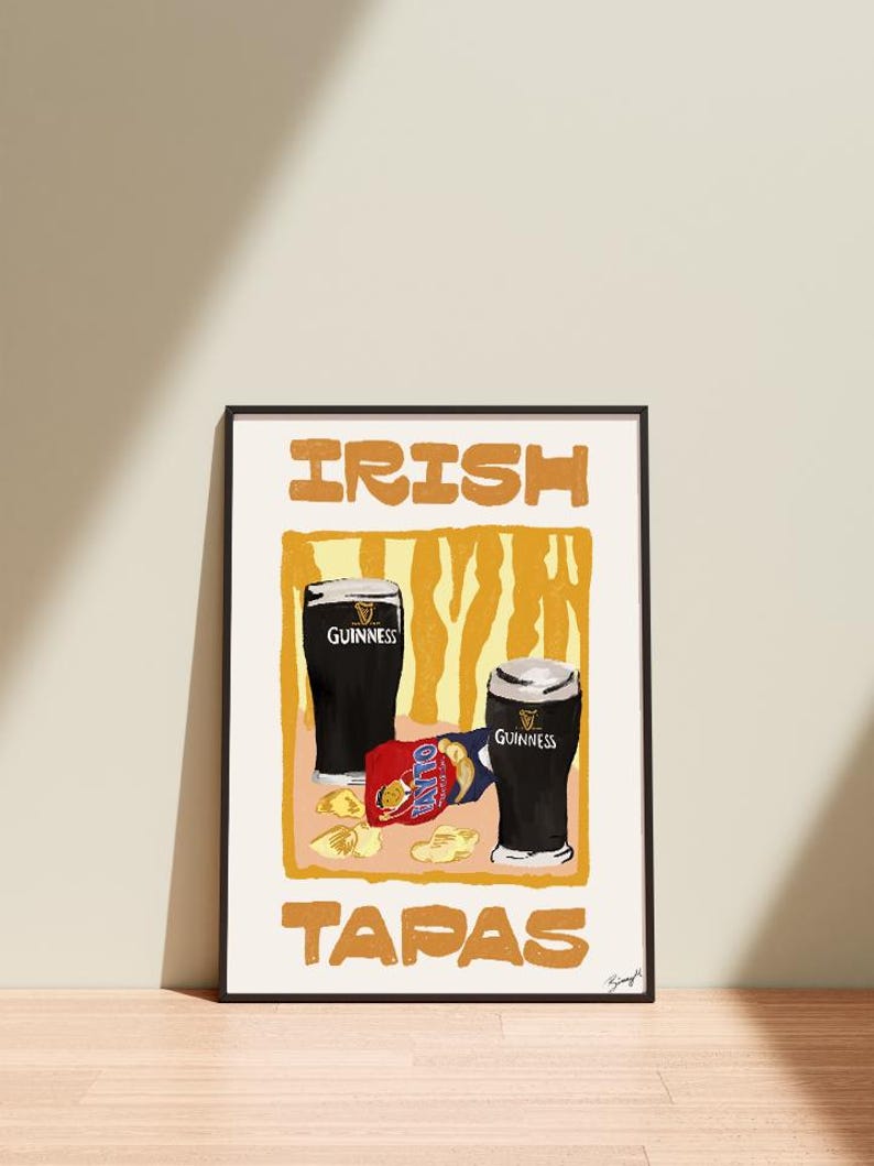May include: Framed print with two pints of Guinness and a packet of olives. The words "IRISH TAPAS" are printed in orange block letters. The background is a yellow and orange abstract design.