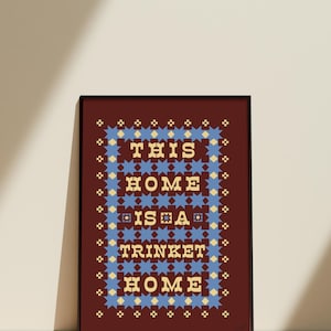 以下が含まれることがあります： 「THIS HOME IS A TRINKET HOME」の文字がスタイリッシュなフォントで描かれた、額装されたアートプリント。テキストは、濃い赤色の背景に青と黄色の星模様で囲まれています。フレームは黒色です。