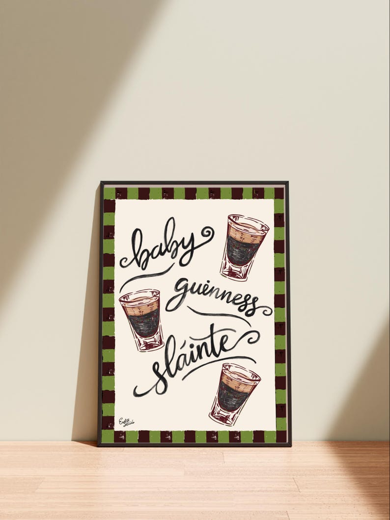 Puede incluir: Una impresi&oacute;n art&iacute;stica enmarcada con las palabras "baby guinness sl&aacute;inte" en escritura cursiva, acompa&ntilde;ada de ilustraciones de tres chupitos de baby Guinness. La impresi&oacute;n tiene un fondo crema y un borde a cuadros verde y marr&oacute;n.