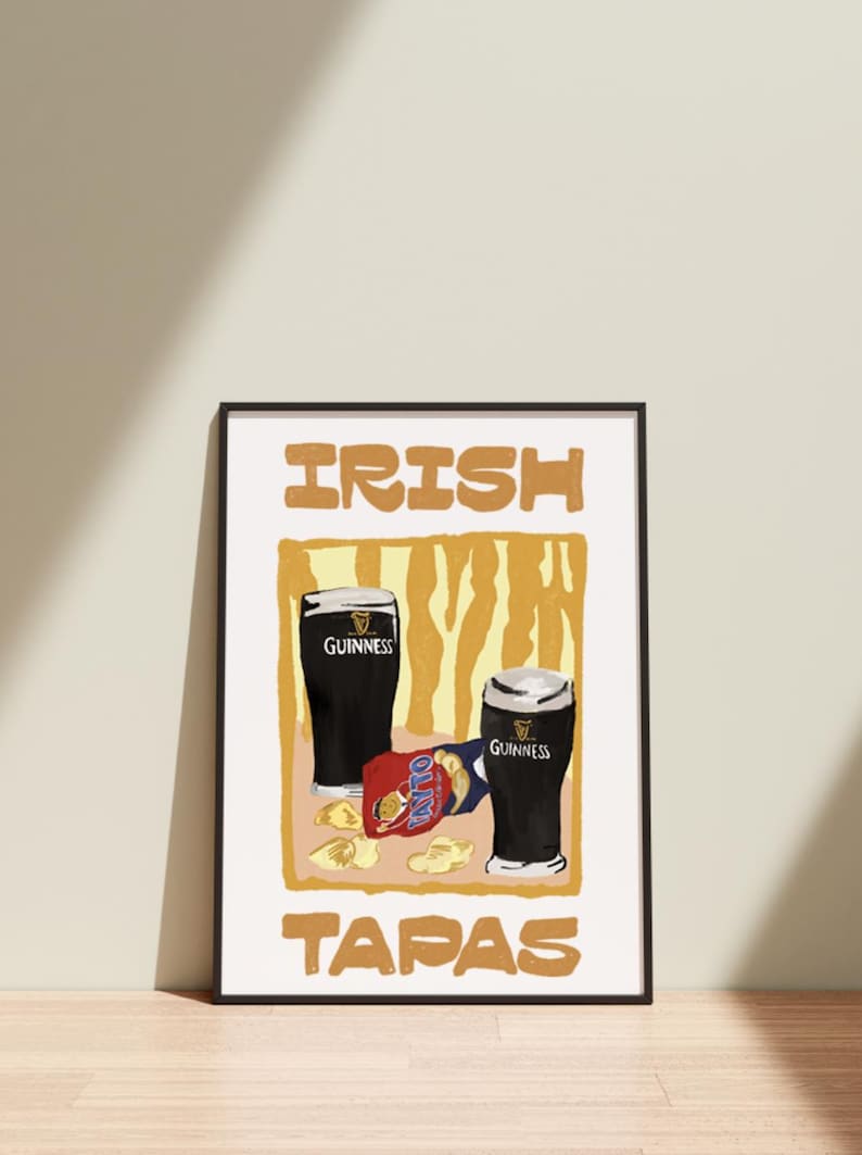May include: Framed print with two pints of Guinness and a packet of crisps. The words "IRISH TAPAS" are in a bold font. The background has a yellow and brown design. A black frame surrounds the print.