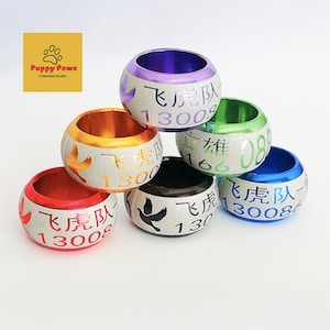 May include: A collection of colorful, metallic rings with Chinese characters and numbers. Each ring has a different color, including red, gold, purple, green, black, and blue. The rings are decorated with a bird design.