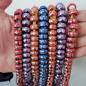 May include: A selection of multi-coloured metal bird bands in red, orange, blue, and purple. Each band is printed with a number and Chinese characters. The bands are strung together, forming a bright display.
