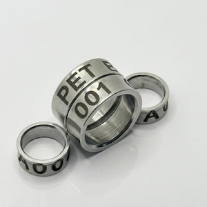 May include: Three silver-toned metal rings with a smooth, polished finish. The larger central ring features the engraved text PET and 001. The two smaller rings on either side also display partial engraved characters, including the letter A and 00.