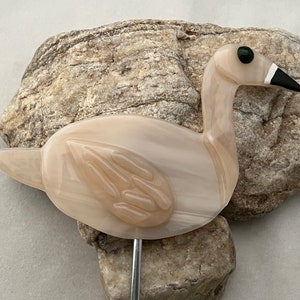 May include: A white glass swan figurine with a black beak and green eye. The swan is perched on a metal stake.