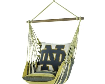 May include: A hanging chair with a wooden bar and beige rope. The chair has a striped pattern in yellow, gray, and white. A pillow with the Notre Dame logo in navy blue and gold rests inside the chair.