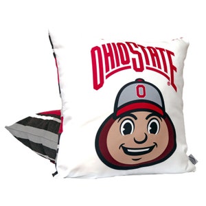 May include: White pillow with a red and gray Ohio State mascot graphic. The mascot is wearing a red and gray baseball cap with a white "O" on it. The text "Ohio State" is in red above the mascot.
