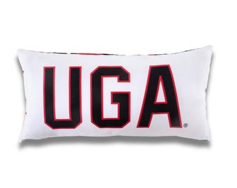 以下が含まれることがあります： 白い長方形の枕で、大きな黒いブロック文字で「UGA」の文字が赤色の縁取りで描かれています。枕は装飾品で、ベッドやソファ用です。背景は白です。