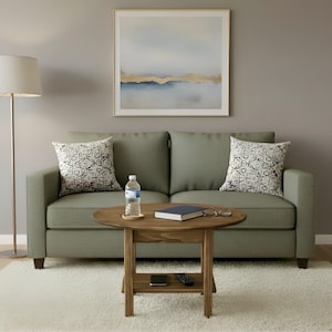 May include: A sage green two-cushion sofa with two patterned throw pillows, a round wooden coffee table with a lower shelf, a clear plastic water bottle, a closed book, a pair of glasses, a remote control, and a smartphone on the table.